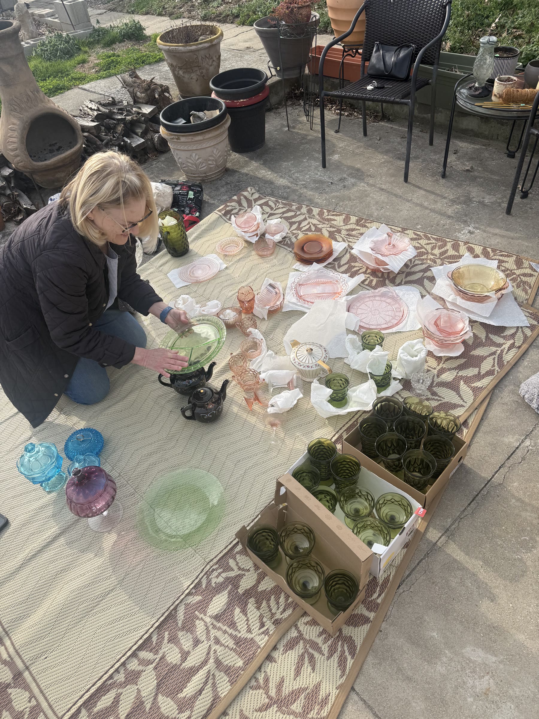 A woman carefully arranging colorful Depression glass for an outdoor estate sale
